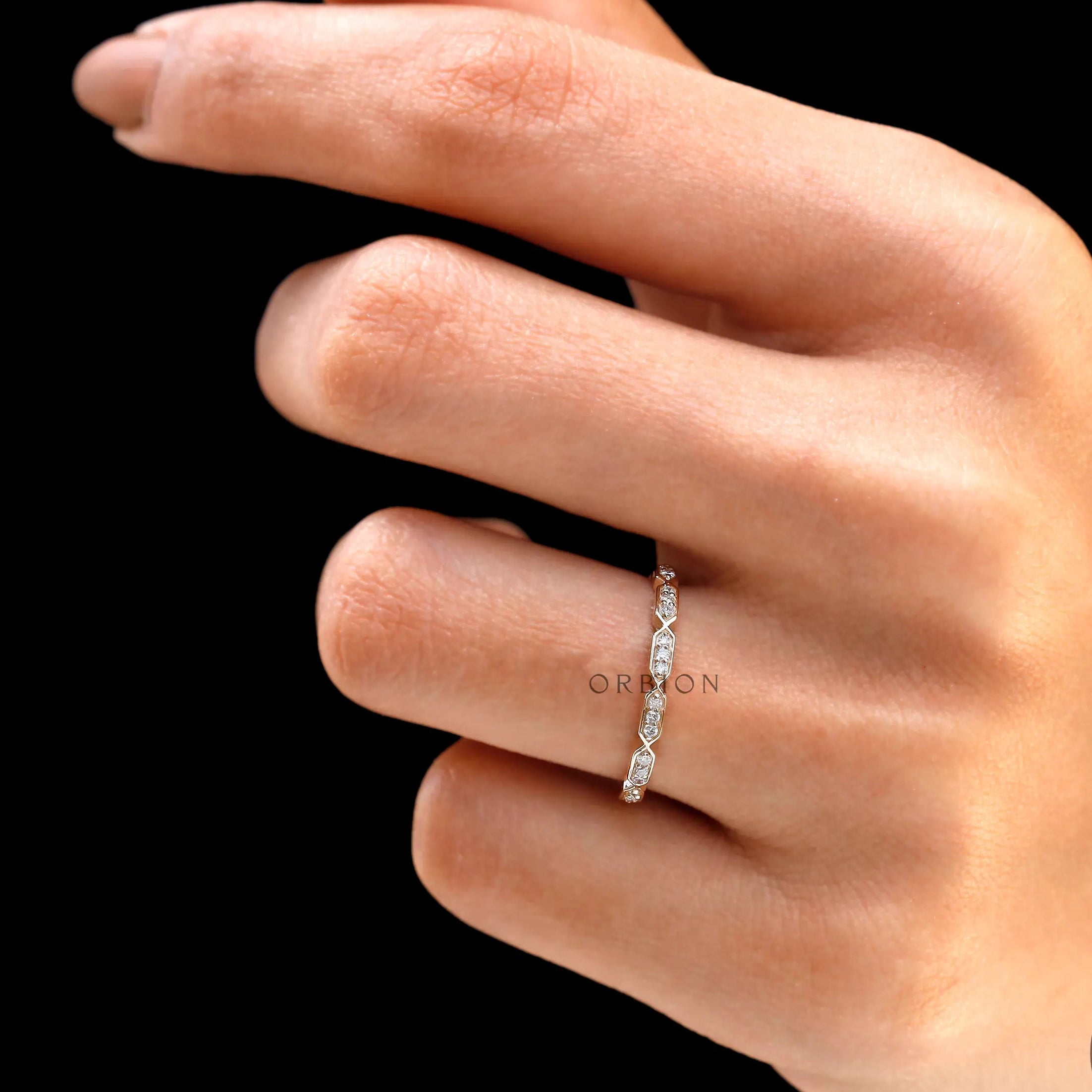 Hand wearing dainty geometric diamond stacking ring on black background