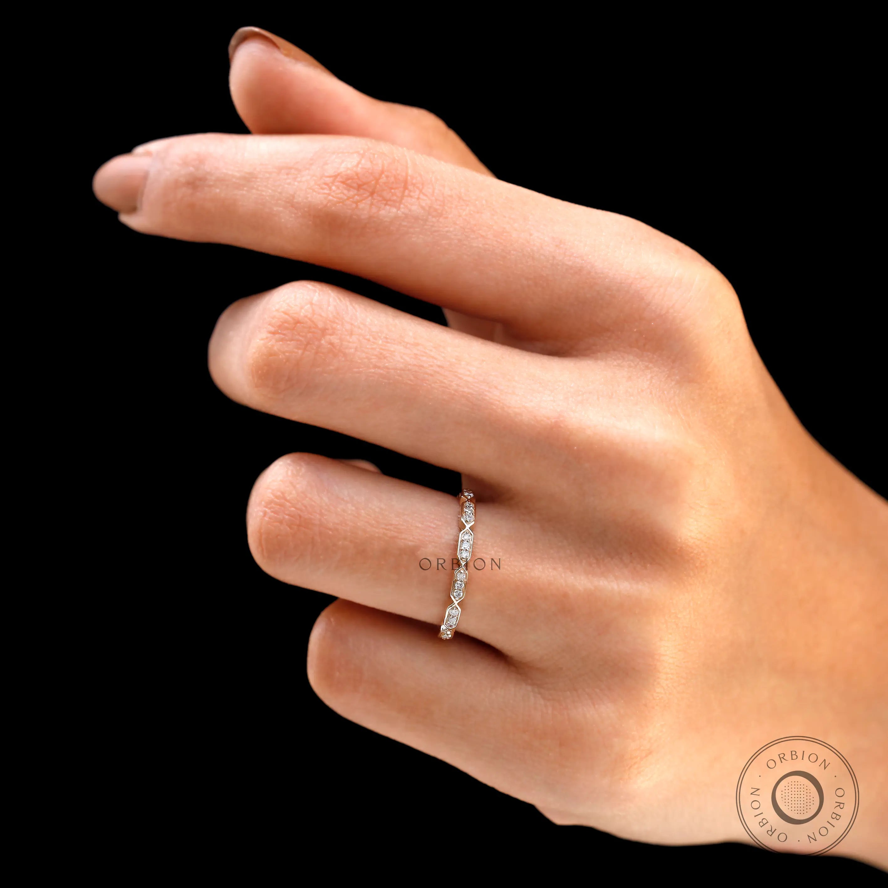 Hand wearing dainty geometric diamond stacking ring on black background