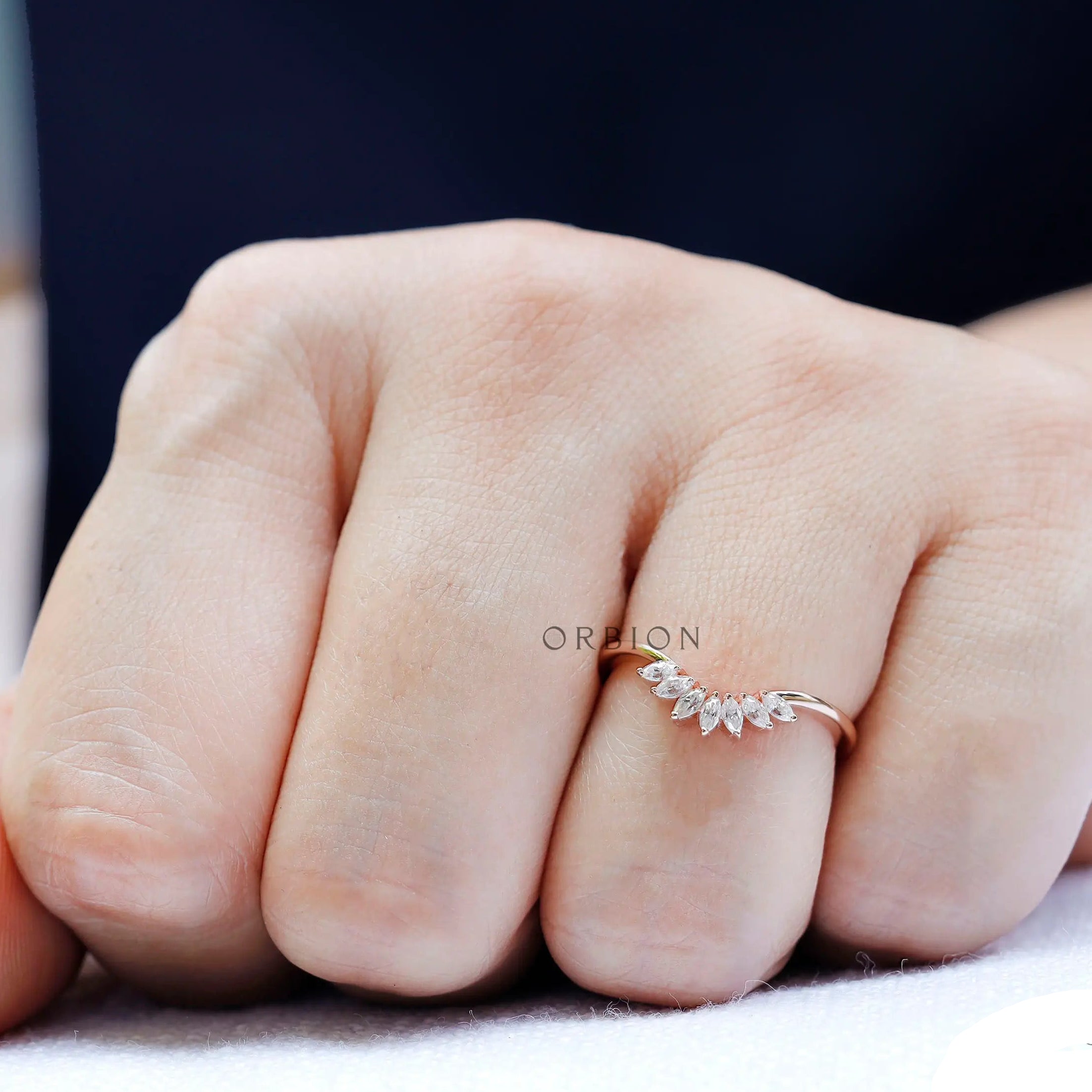 Close-up of marquise moissanite curved band showing delicate sparkle on hand