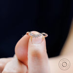 Finger-held close-up of curved nesting band with marquise in rose gold