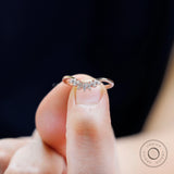 Finger-held close-up of curved nesting band with marquise in rose gold