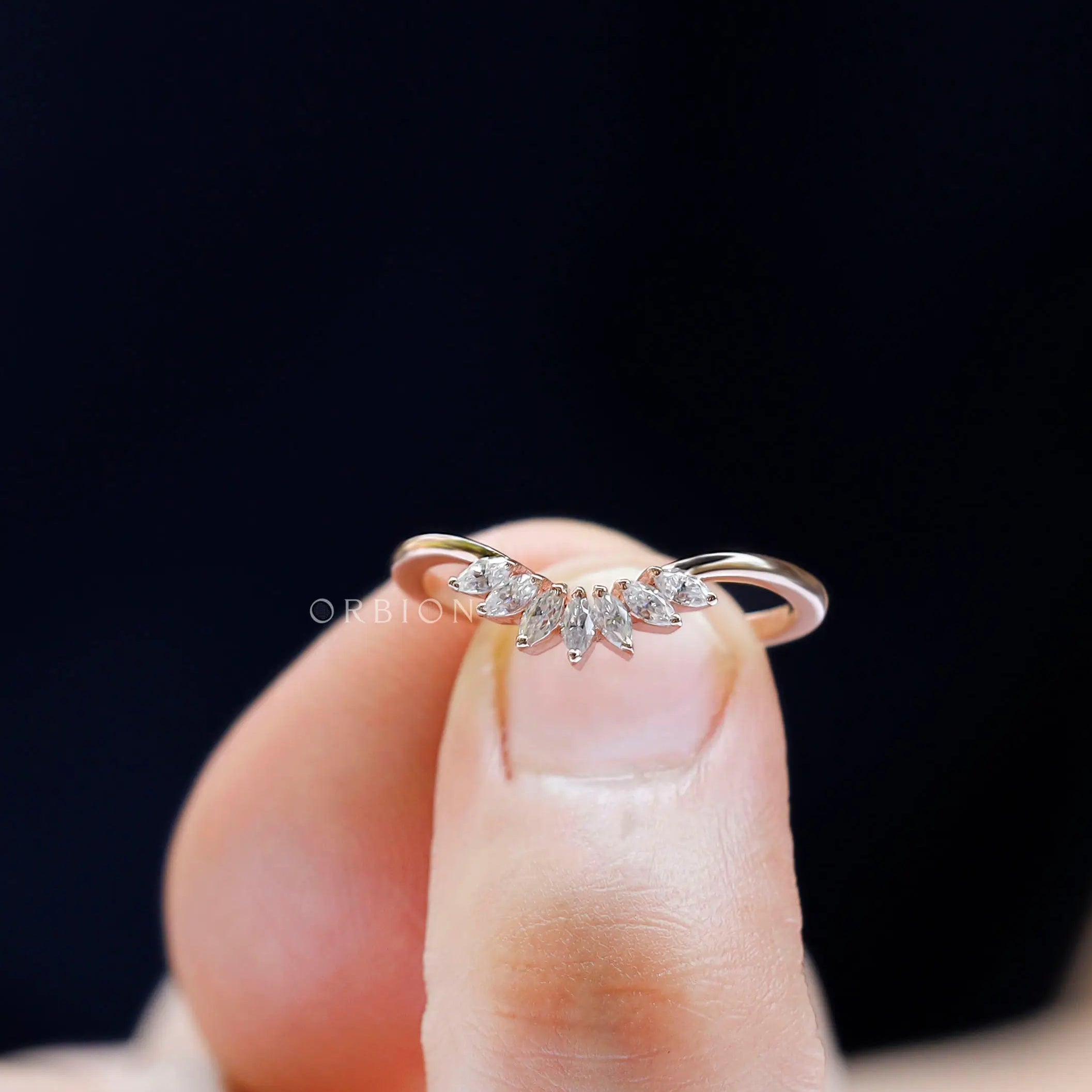 Finger-held close-up of curved nesting band with marquise in rose gold