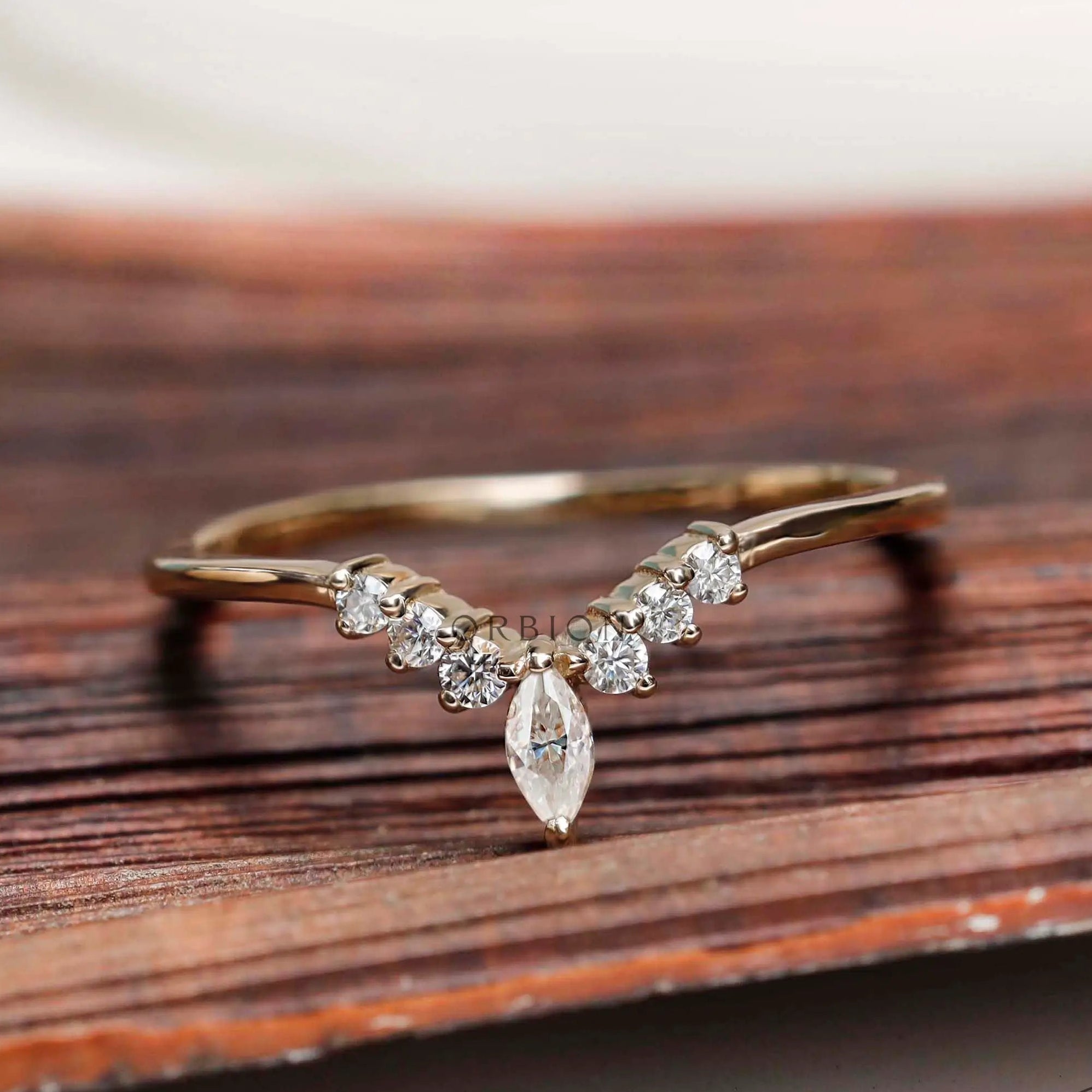 Front view of marquise and round cut chevron contour moissanite wedding band on wooden surface