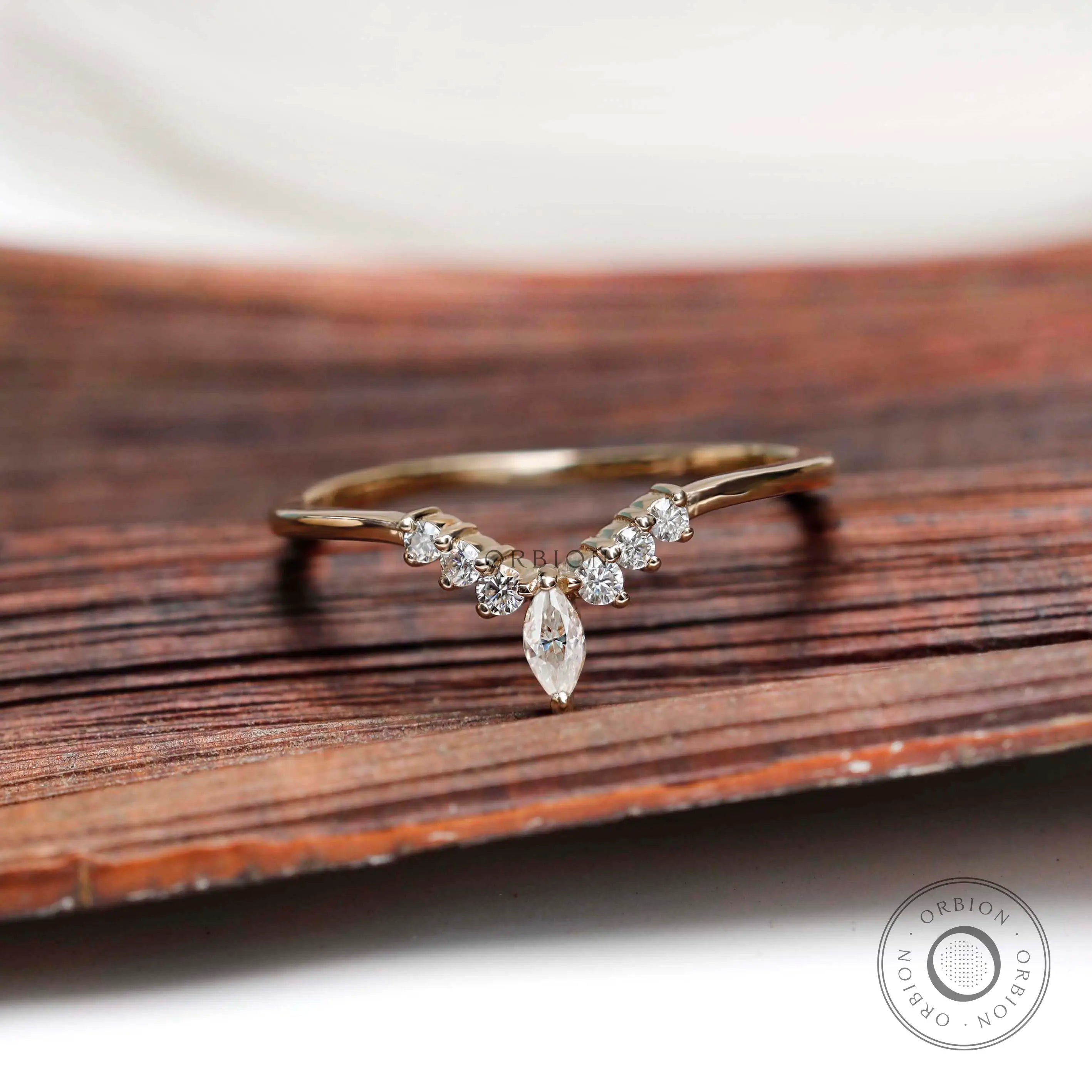 Front view of marquise and round cut chevron contour moissanite wedding band on wooden surface