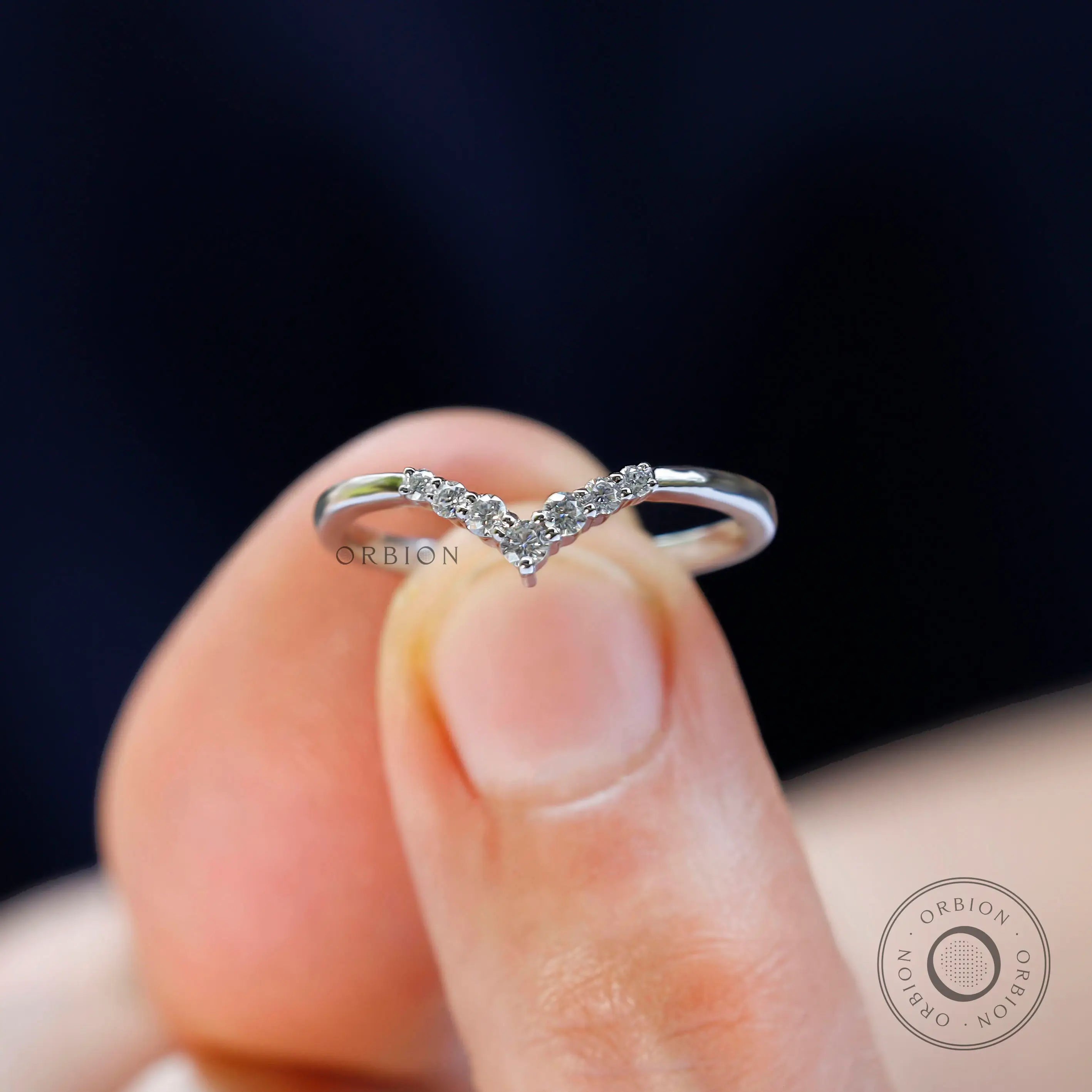 Chevron wedding band held on fingertip highlighting slim design