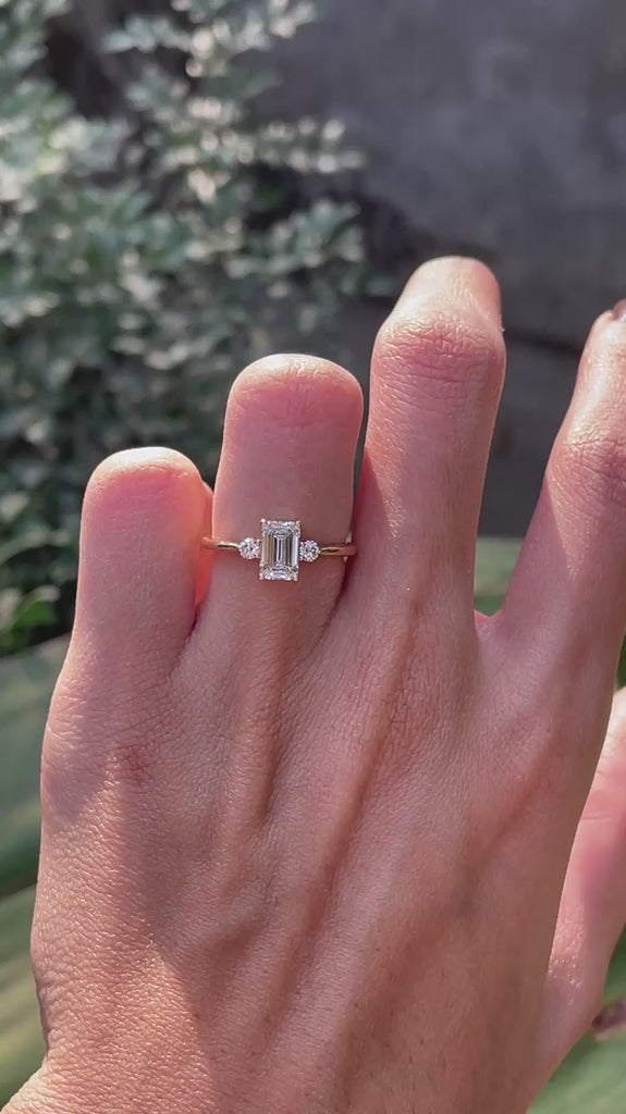 Delicate emerald cut engagement ring with round side stones on hand video