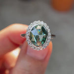 Oval rose cut bluish green moissanite halo engagement ring in 10K white gold rotating view highlighting brilliance and halo detail