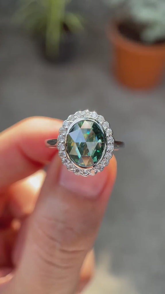 Oval rose cut bluish green moissanite halo engagement ring in 10K white gold rotating view highlighting brilliance and halo detail