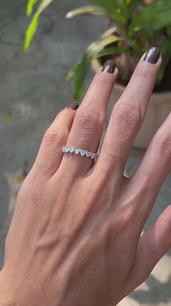 Close up view of heart cut moissanite half eternity wedding band worn on hand