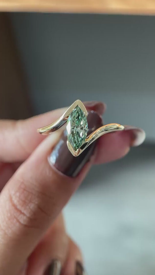 Rotating view light blue green marquise lab diamond half bezel ring.