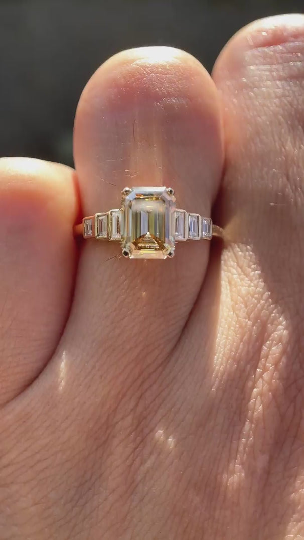 Emerald cut light champagne moissanite 3 stone engagement ring in yellow gold shown in rotating view