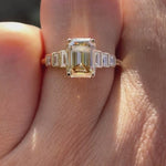 Emerald cut light champagne moissanite 3 stone engagement ring in yellow gold shown in rotating view