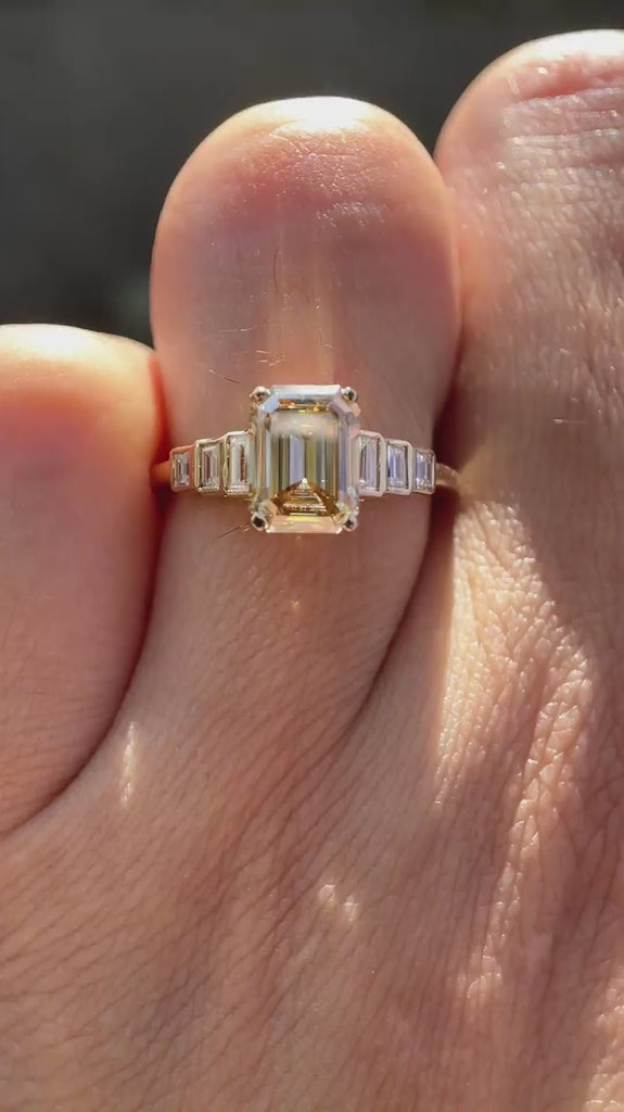 Emerald cut light champagne moissanite 3 stone engagement ring in yellow gold shown in rotating view