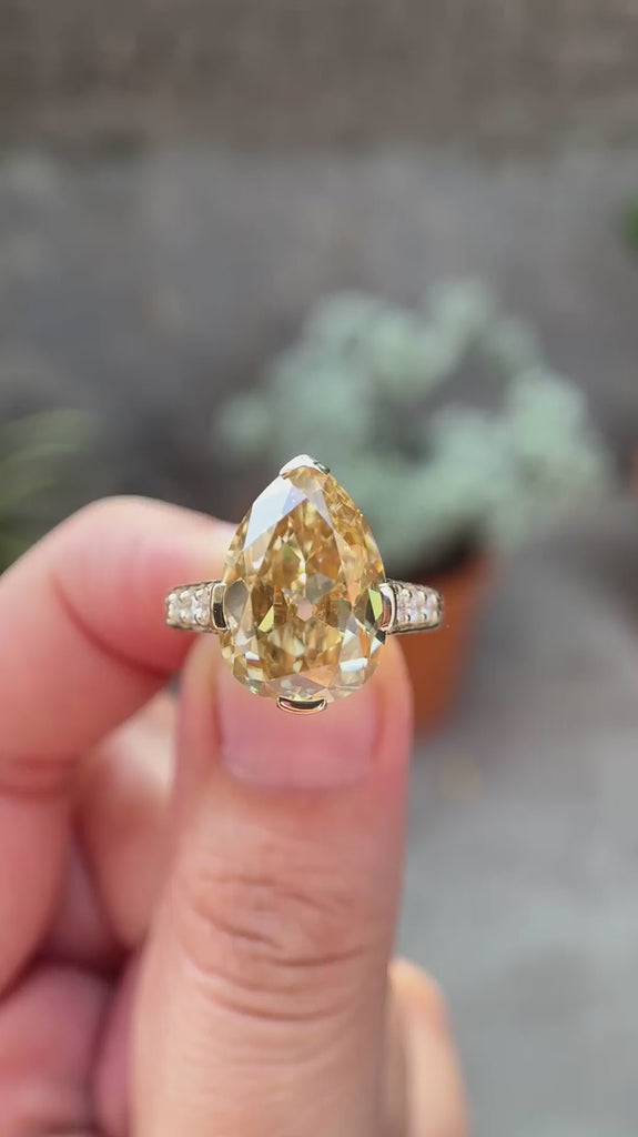 Hand worn pear Old Mine cut light champagne moissanite ring showing sparkle, pave band detail, and side profile in natural lighting