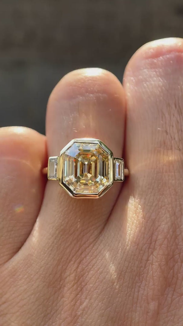 Emerald step cut light champagne moissanite bezel set three stone ring rotating view