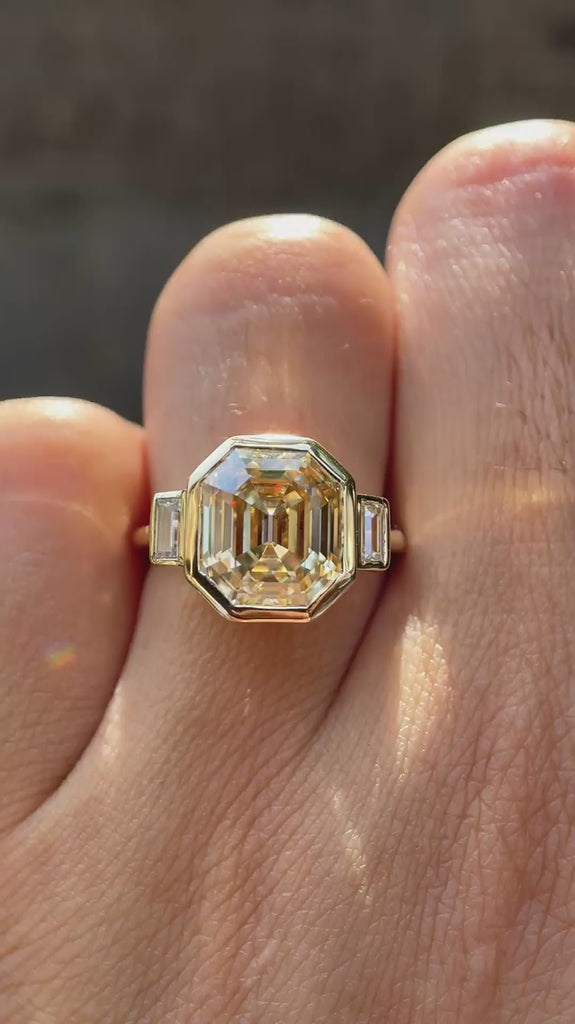 Emerald step cut light champagne moissanite bezel set three stone ring rotating view