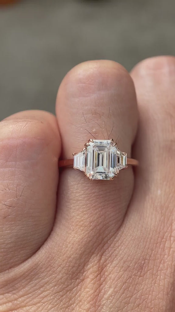Emerald cut moissanite three stone ring rotating view highlighting trapezoid side stones and step cut brilliance
