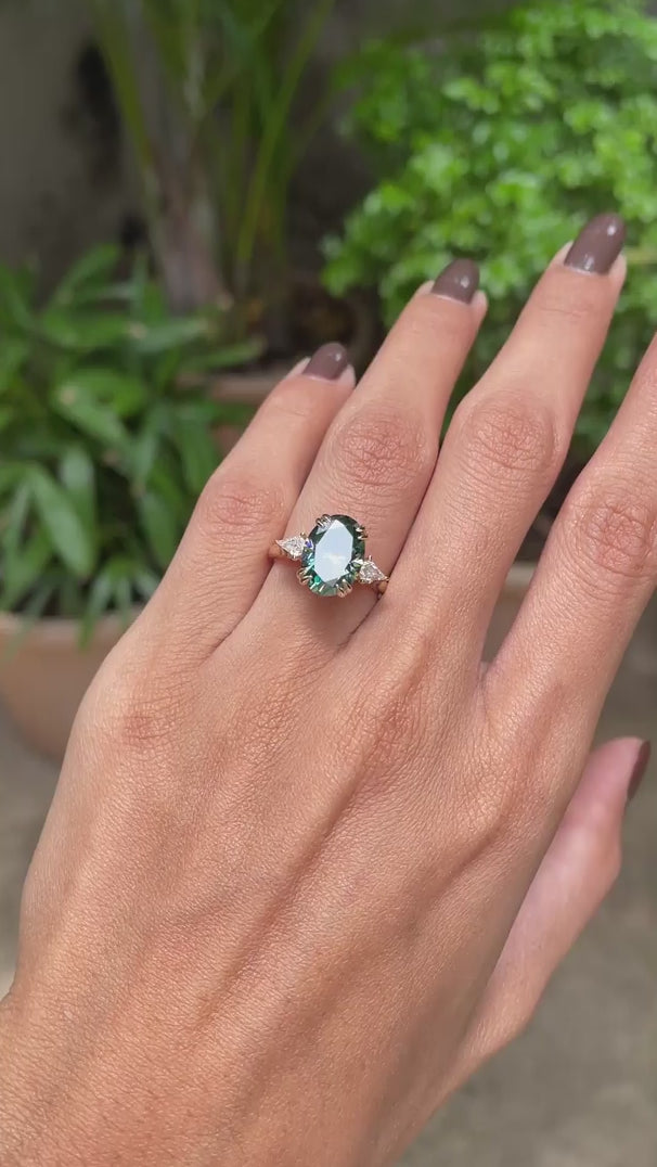 14k yellow gold cathedral ring featuring oval blue green moissanite with three stones and kite accents.