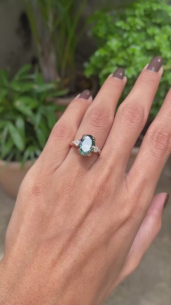 14k yellow gold cathedral ring featuring oval blue green moissanite with three stones and kite accents.