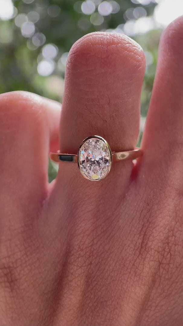 Rotating view of oval bezel set solitaire engagement ring on hand in natural light