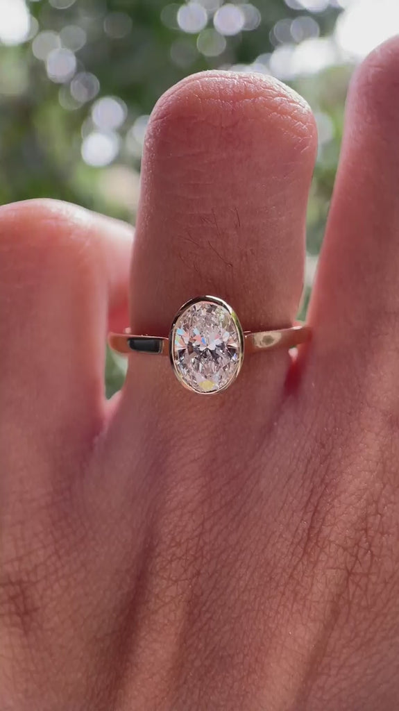 Rotating view of oval bezel set solitaire engagement ring on hand in natural light