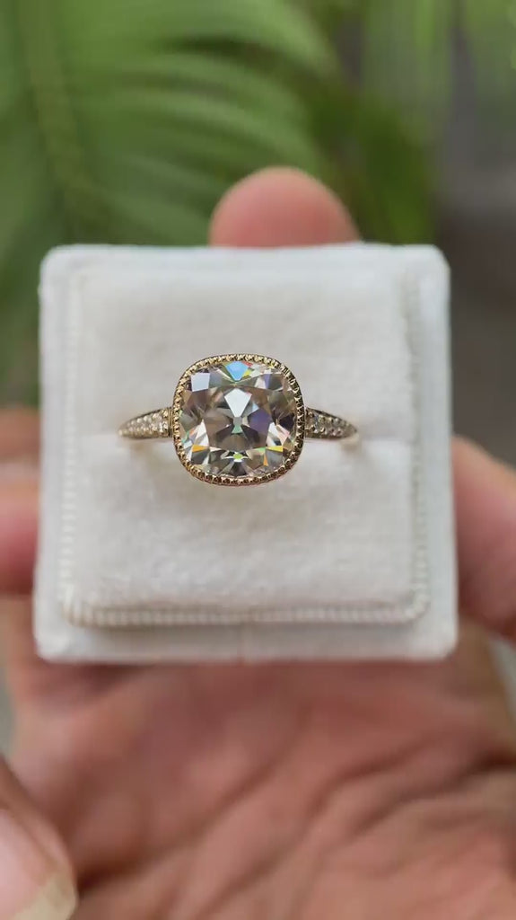 A close-up view of the Bezel Set Cushion Cut Moissanite Engagement Ring in 14K Yellow Gold, highlighting the 3 CT Moissanite center stone and round side stones, showcasing the ring from multiple angles.