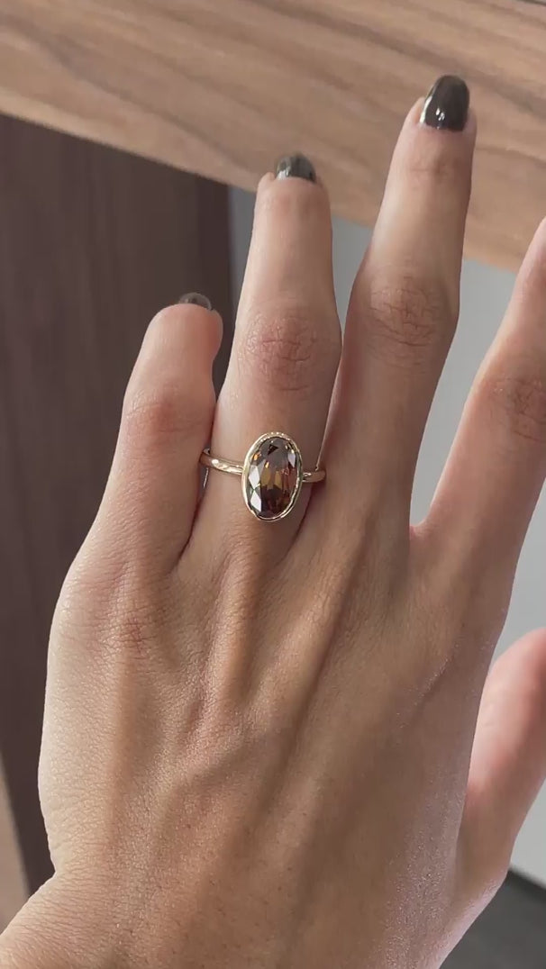 Dark champagne oval Old Mine Cut moissanite bezel set engagement ring in 14K yellow gold rotating view