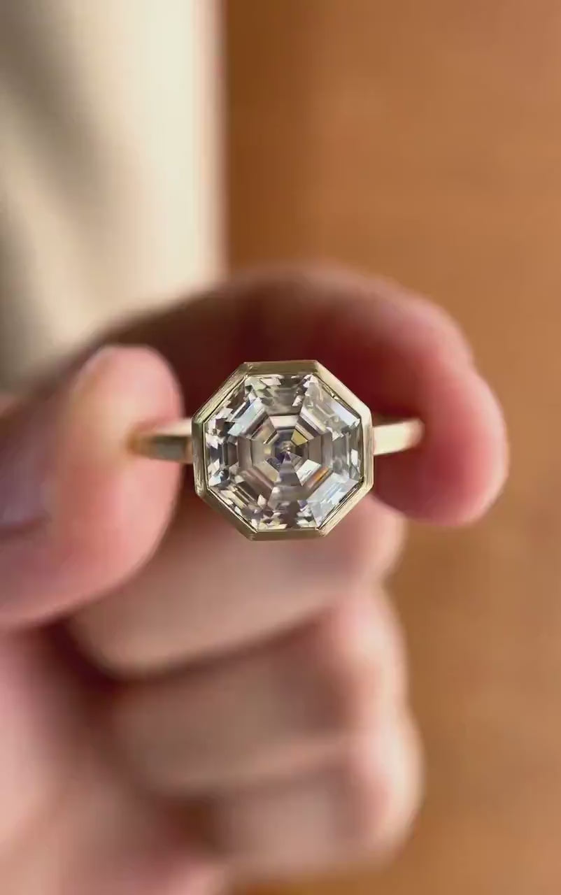 Moissanite octagon step cut bezel set cathedral style solitaire ring in 10K yellow gold