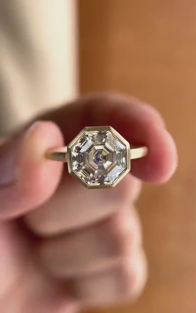 Moissanite octagon step cut bezel set cathedral style solitaire ring in 10K yellow gold