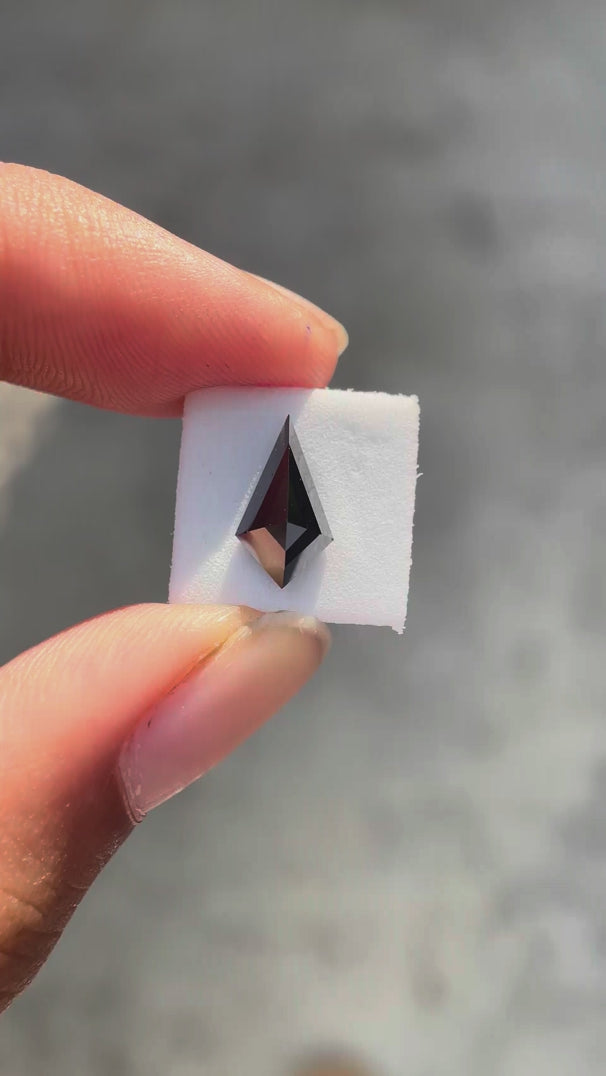 Kite step cut black moissanite rotating to showcase sharp facets and deep reflective surface