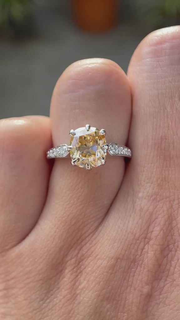Moissanite engagement ring with an elongated cushion cut center stone, showcasing round brilliant cut side stones in a 18K yellow gold setting.