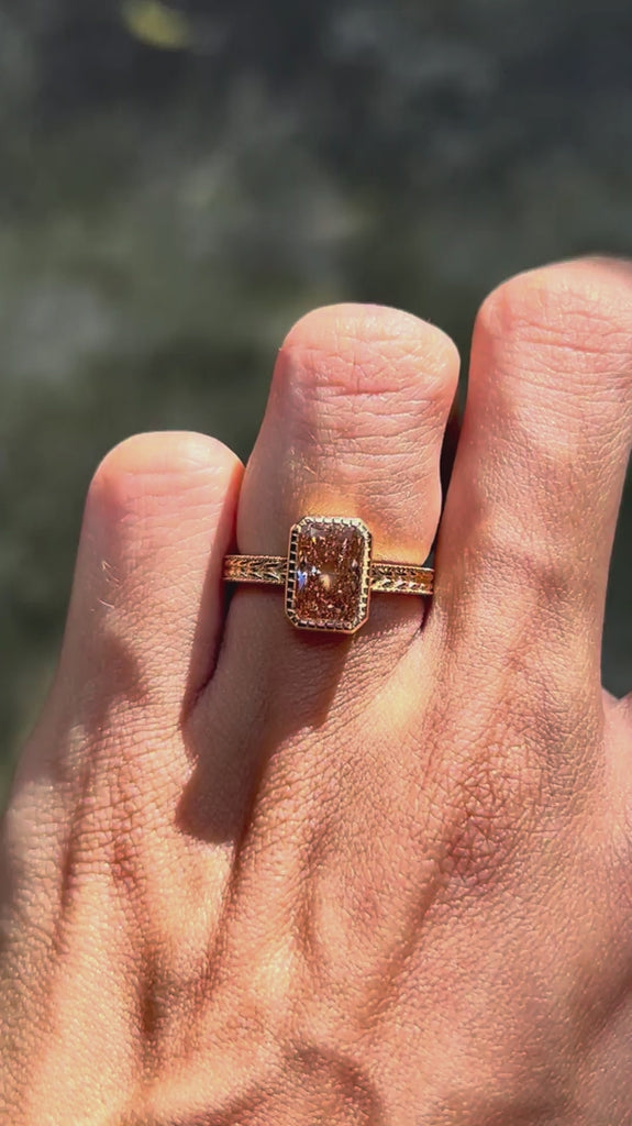 Nature inspired pink diamond engagement ring featuring intricate leaf engraving and bezel setting in 18k yellow gold