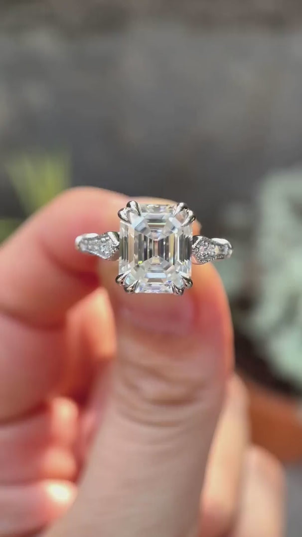 Rotating view of emerald cut moissanite cathedral with vintage look ring held on fingers 