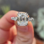 Rotating view of emerald cut moissanite cathedral with vintage look ring held on fingers 