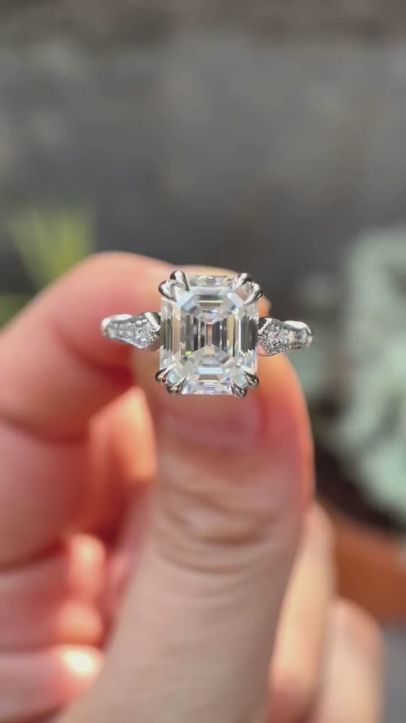 Rotating view of emerald cut moissanite cathedral with vintage look ring held on fingers 