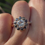 Hand worn vintage halo moissanite ring with black accent stones showing sparkle, contrast, and side profile in natural lighting